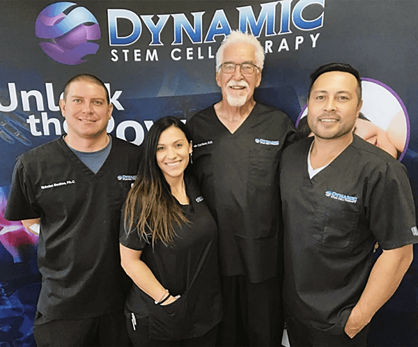 Four people in matching black scrubs stand in front of a "Dynamic Stem Cell Therapy" banner, smiling at the camera. Four people in matching black scrubs stand in front of a "Dynamic Stem Cell Therapy" banner, smiling at the camera.